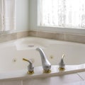 Square Bathtub with with gold and silver faucet beside an arched window with curtain