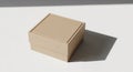 A square, beige cardboard box sits on a smooth white surface. The box appears closed Royalty Free Stock Photo