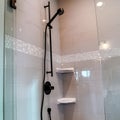 Square Black round shower head on tile wall of shower stall with hinged glass door