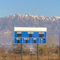 Square Blue and white baseball scoreboard above the chain link fence at a sports field