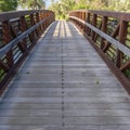 Square Bridge with wood deck and rusty metal railing over a lake with grassy shore