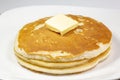 A square of butter laying onto of a stack of golden pancakes on the kitchen table waiting to be eaten Royalty Free Stock Photo