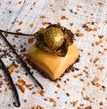 Square candy in caramel glaze decorated with chocolate and a ball covered with edible gold. Sweetness on a light wood background