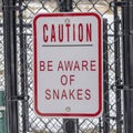 Square Caution Be Aware of Snakes sign on the chain link fence of a recreational park