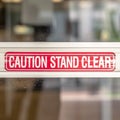Square Caution Stand Clear sign on the metal plate of the glass door of a building