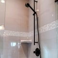 Square crop Black round shower head on tile wall of shower stall with hinged glass door