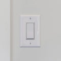 Square Electrical rocker light switch on white wall against blurry door background