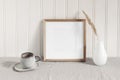 Square empty wooden frame mockup with modern ceramic vase, dry grass, cup of coffee on table. White beadboard wainscot Royalty Free Stock Photo