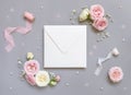 Square envelope between pink roses and pink silk ribbons on grey top view, wedding mockup
