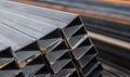 Square flat-rolled pipe metal profile in packs at the warehouse of metal products. Weathered metals profiles for