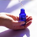 Square format of blue glassy bottle with pipette full of facial skin care translucent liquid serum for treatment. Spa