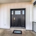 Square frame Black wooden front door with glass panes against panelled exterior wall of home