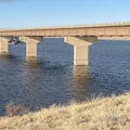 Square frame Bridge across blue lake with views of snow covered hills and cloudy blue sky