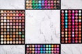 Frame made of colorful cosmetic eyeshadow palettes on white marble background. Flat lay