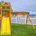 Square frame Playground on a backyard with view of homes and cloudy sky beyond the fence