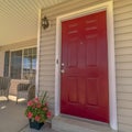 Square frame Shiny red wooden front door of a home with wicker chairs on the sunlit porch Royalty Free Stock Photo