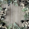 Square frame of silver green leaves and white berries over gray wood