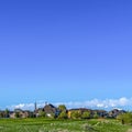 Square frame Vast grassy terrain with houses under blue sky and puffy clouds on a sunny day Royalty Free Stock Photo