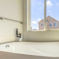 Square Glossy bathtub and wall mounted towel rod inside a bathroom lit by sunlight