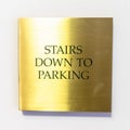 Square Gold plated sign that reads Stairs Down To Parking against white interior wall Royalty Free Stock Photo