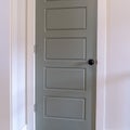 Square Gray door with matte black door knob and white door frame against wall