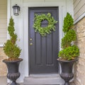 Square Gray front door of a home with green wreath and flanked by tall potted plants Royalty Free Stock Photo