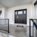 Square Home entrance with front porch and black front door against white panelled wall Royalty Free Stock Photo