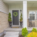 Square Home facade with stairs leading to porch with pillars and gray door with wreath