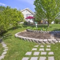 Square Landscaped grassy yard of home with lush trees and decorative concrete stones