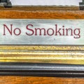 Square No Smoking sign above mail drop slot with black tape against brown wood door