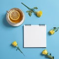 Square notepad on springs with white kraft paper, yellow rose and cup of tea are on a blue background. Royalty Free Stock Photo