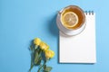 Square notepad on springs with white kraft paper, yellow rose and cup of tea are on a blue background. Royalty Free Stock Photo