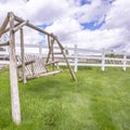 Square Old wooden garden swing on lush green grasses inside white picket fence Royalty Free Stock Photo