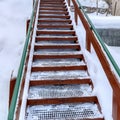 Square Outdoor stairs with grate metal treads and green handrail on snowy winter hill