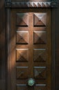 Square patterned door panel in bright sunlight. Natural wooden doorway with shiny vintage round ornate doorknob.