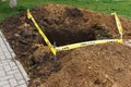 A square pit dug into the soil, next to public sidewalk and fenced with a ribbon, as a sign of danger. Communal service works,