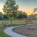 Square Playground and benches at a park against trees mountain and sky at sunset