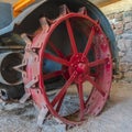 Square Red wheel rim of an and vintage tractor against stone wall of a farm barn