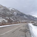 Square Road along steep snowy mountain in Provo Canyon with cloudy sky background