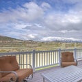 Square Seating area on a home deck with view of road houses mountain and cloudy sky