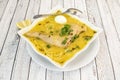 Square shaped bowl of Peruvian chicken broth recipe with noodles, chives and boiled egg