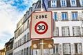 Square shaped 30km/h speed limit zone sign in front residential buildings in background