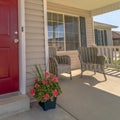 Square Shiny red wooden front door of a home with wicker chairs on the sunlit porch Royalty Free Stock Photo