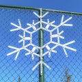 Square Snowflake ornament hanging on a green chain link fence against clear blue sky Royalty Free Stock Photo