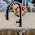 Square Stainless steel sink with two bowls and black curved faucet against fruit basket Royalty Free Stock Photo