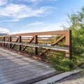 Square Sunny day view of a bridge with wooden deck and metal guardrail over a lake Royalty Free Stock Photo