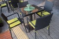 Square table with green decorative round cloth and flowers and four black wicker chairs with yellow padded cushions