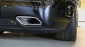 Square tailpipe at the rear right side of a black sports car. Very low plan. The rear bumper, wheel and tailpipe of the packed Royalty Free Stock Photo