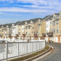 Square Townhouses along road with white fence against scenic blue sky and white clouds