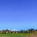 Square Vast grassy terrain with houses under blue sky and puffy clouds on a sunny day Royalty Free Stock Photo